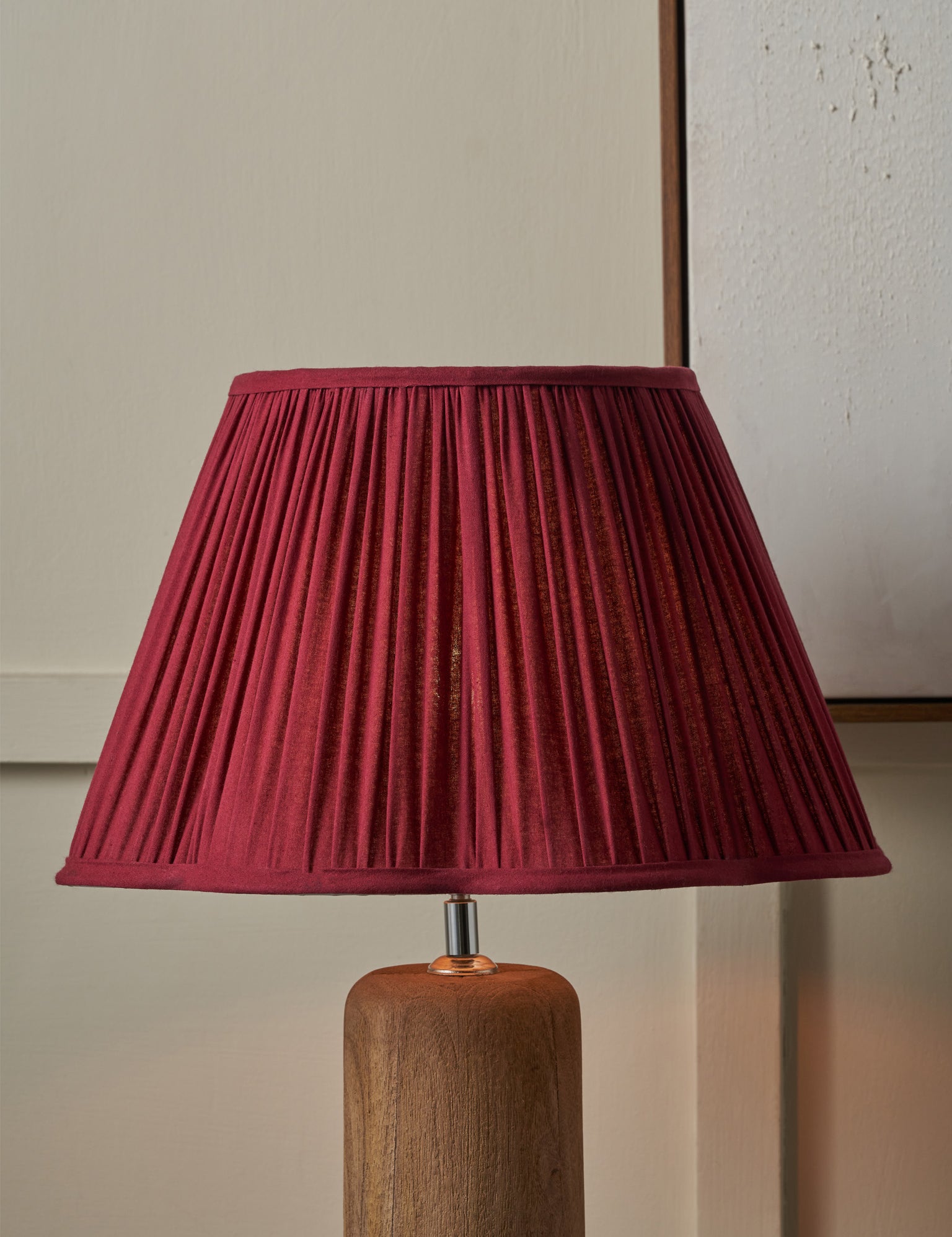 Lamp with a pleated red shade on a wooden base against a neutral wall.