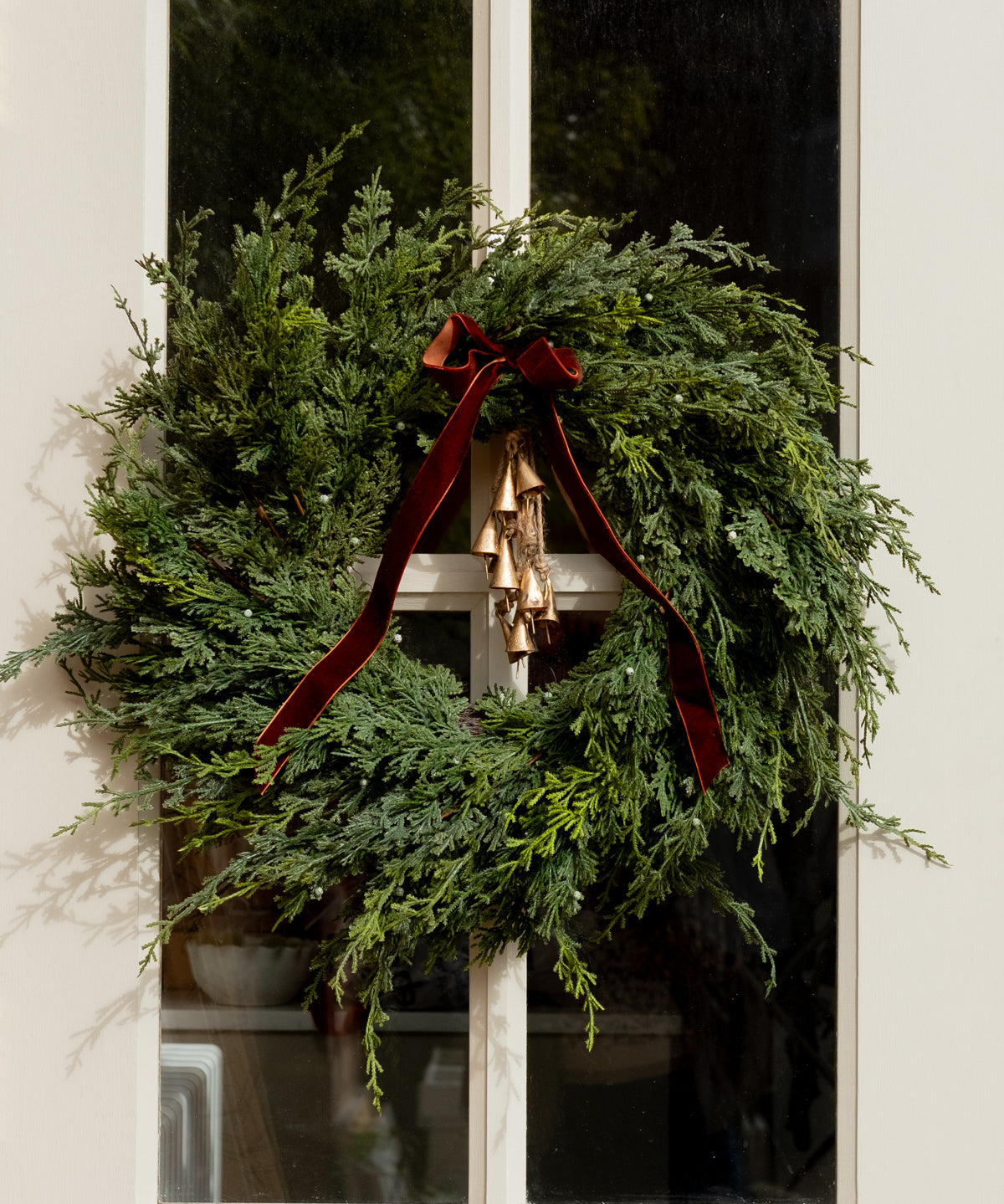 Green wreath with a brown ribbon on a white door with christmas bells