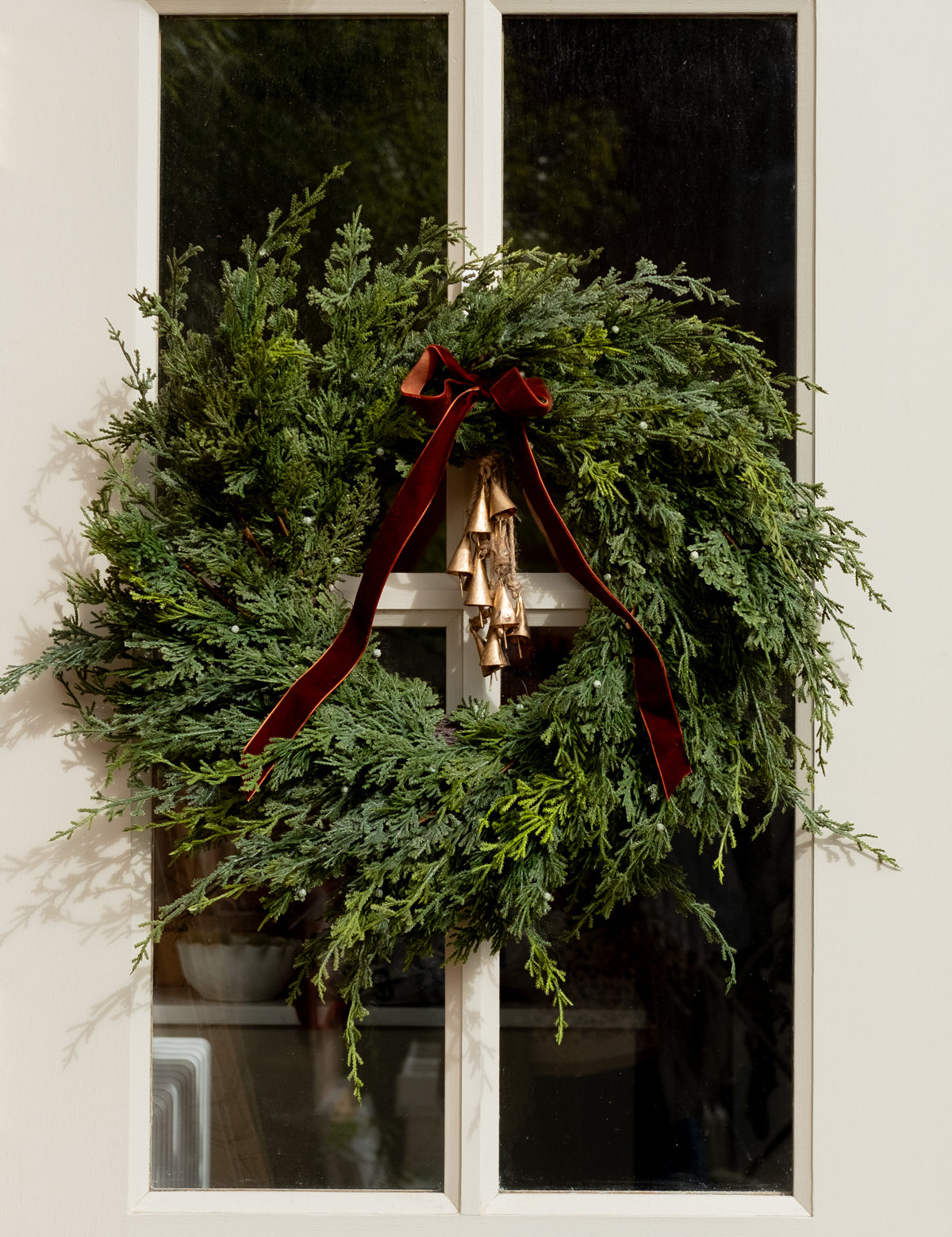 Green wreath with a brown ribbon on a white door with christmas bells