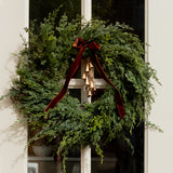 Green wreath with a brown ribbon on a white door with christmas bells