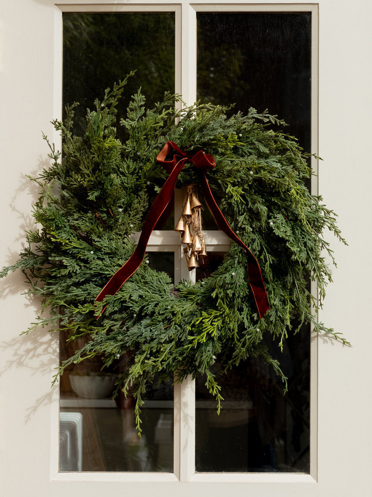 Green wreath with a brown ribbon on a white door with christmas bells