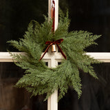 Decorative evergreen wreath with a red ribbon and gold bell on a white door.