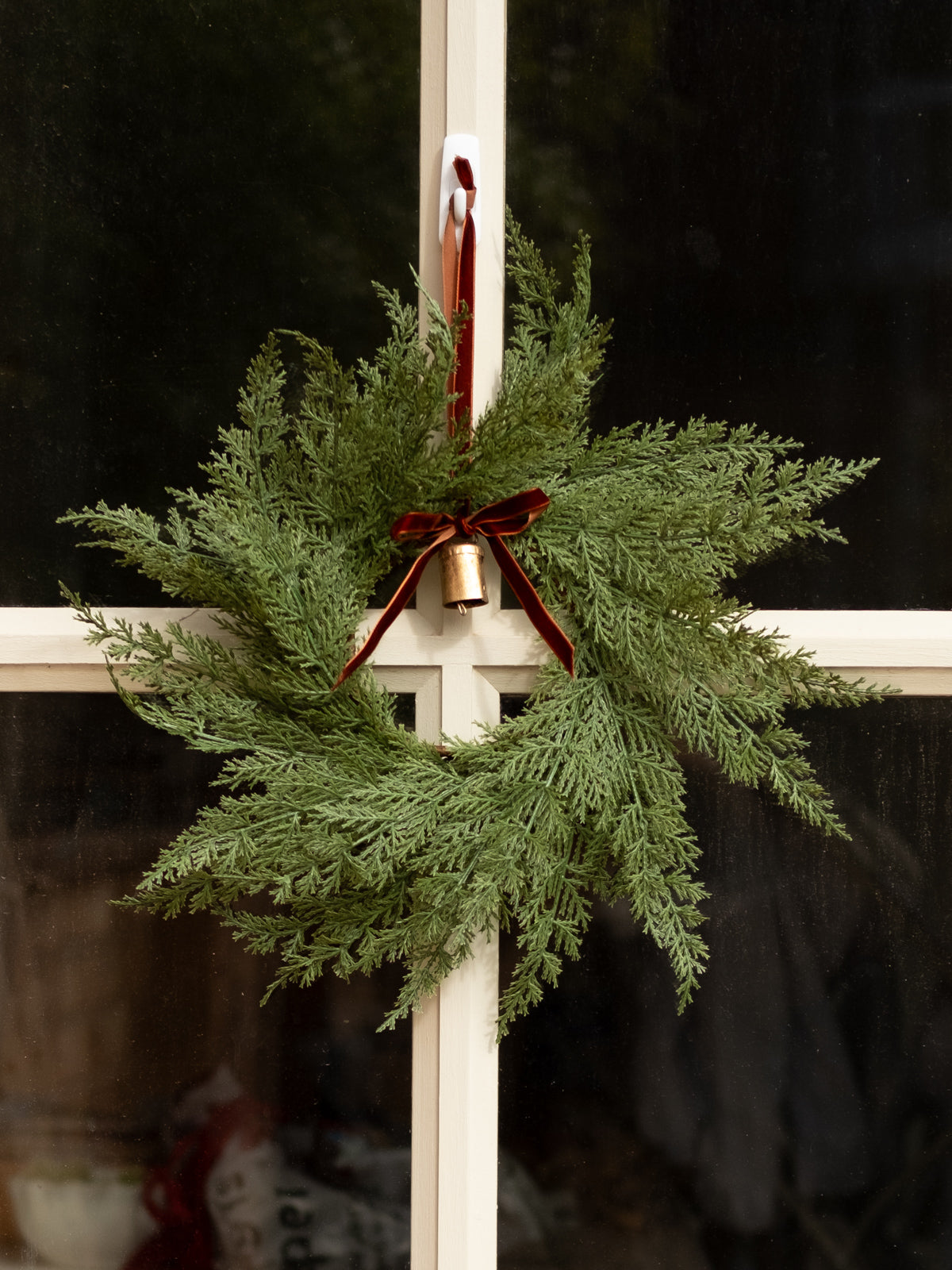 Decorative evergreen wreath with a red ribbon and gold bell on a white door.