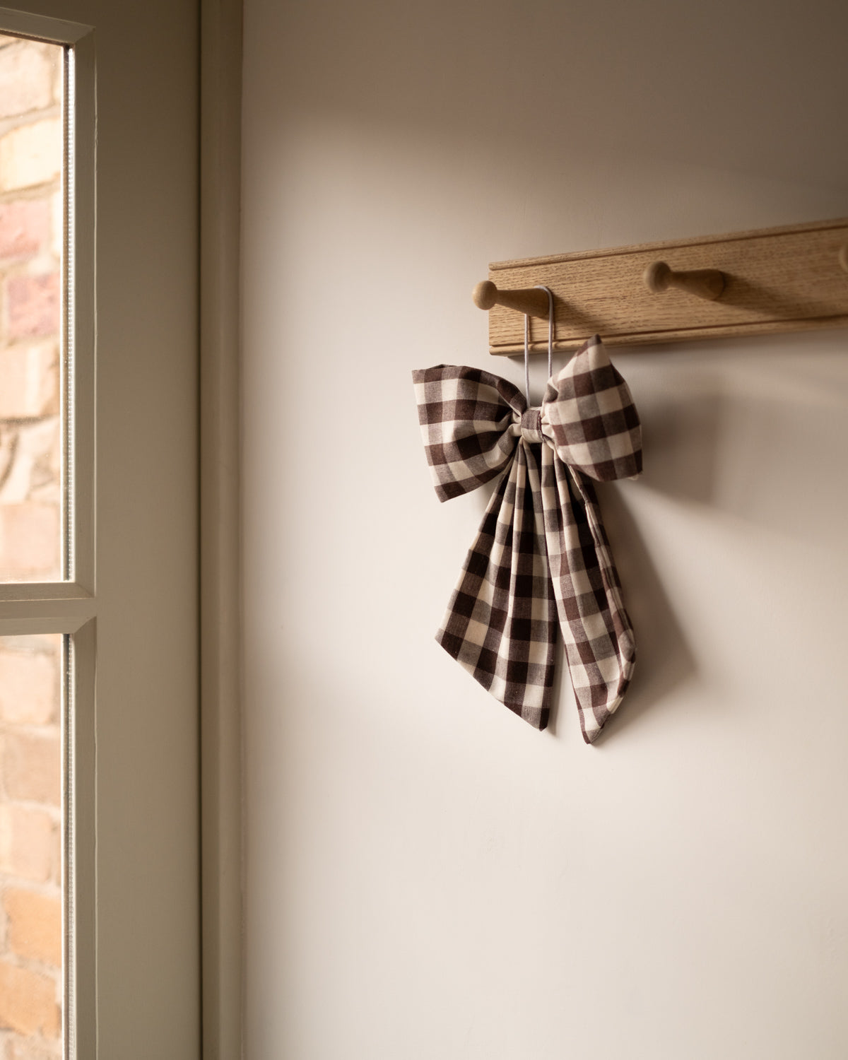 gingham bow hanging on a wooden hook against a neutral wall.
