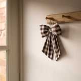 gingham bow hanging on a wooden hook against a neutral wall.