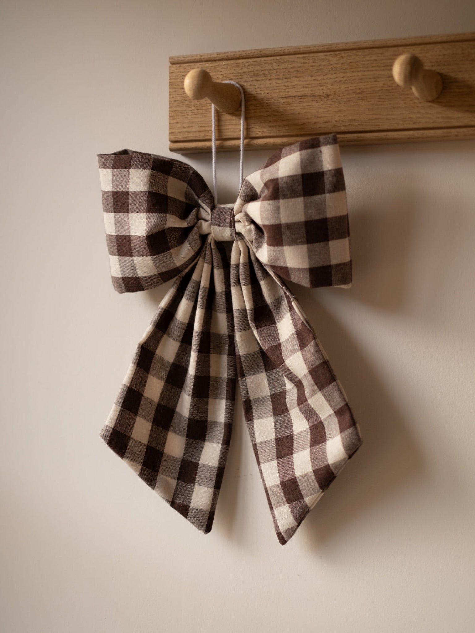 gingham bow tie hanging on a wooden hook against a beige wall.