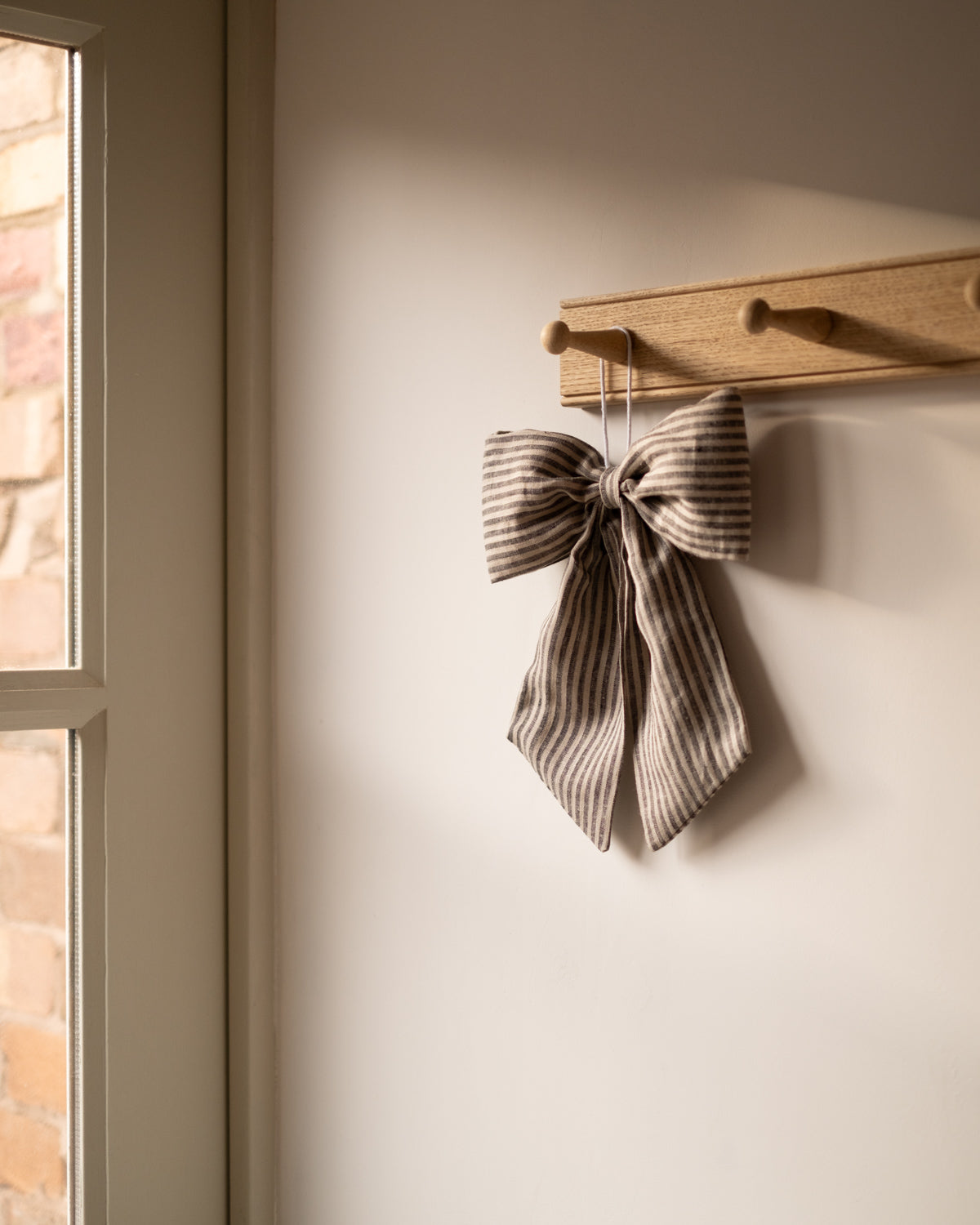 Textured bow decoration hanging on a wooden hook against a neutral wall.