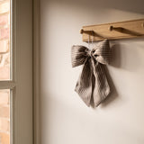 Textured bow decoration hanging on a wooden hook against a neutral wall.