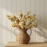 McGee & Co Rattan vase with dried flowers on a wooden surface against a light wooden panel wall