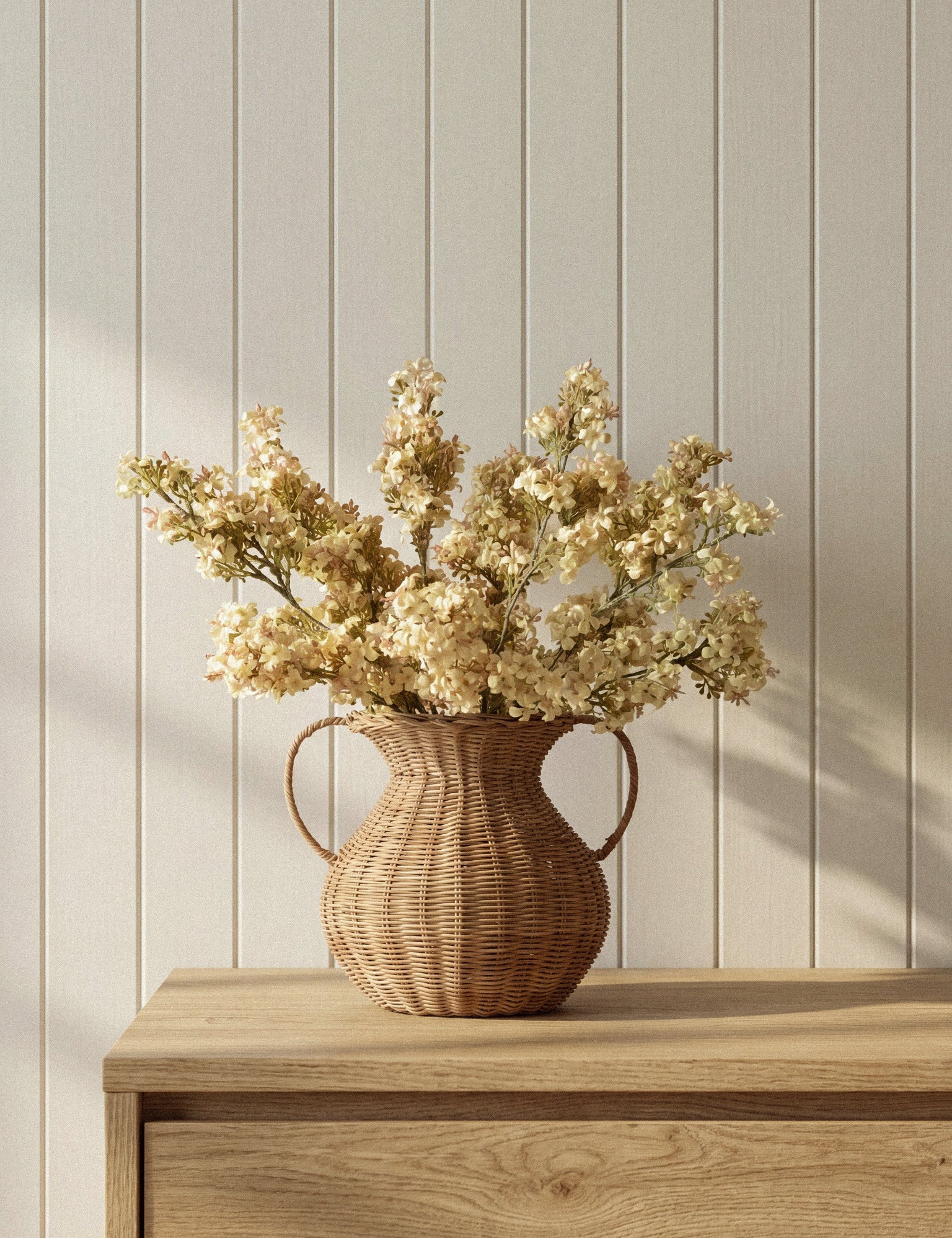 McGee & Co Rattan vase with dried flowers on a wooden surface against a light wooden panel wall