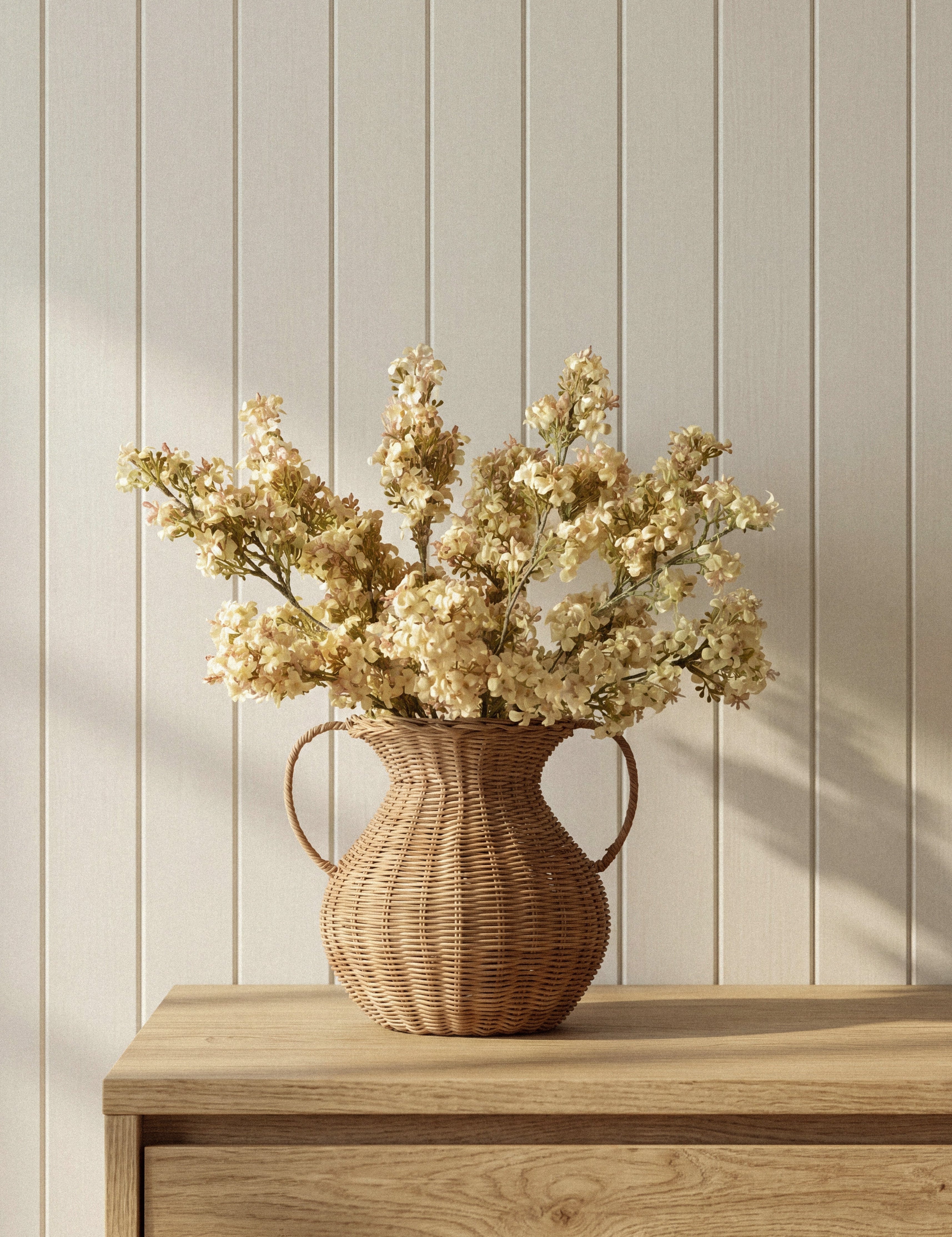 McGee & Co Rattan vase with dried flowers on a wooden surface against a light wooden panel wall