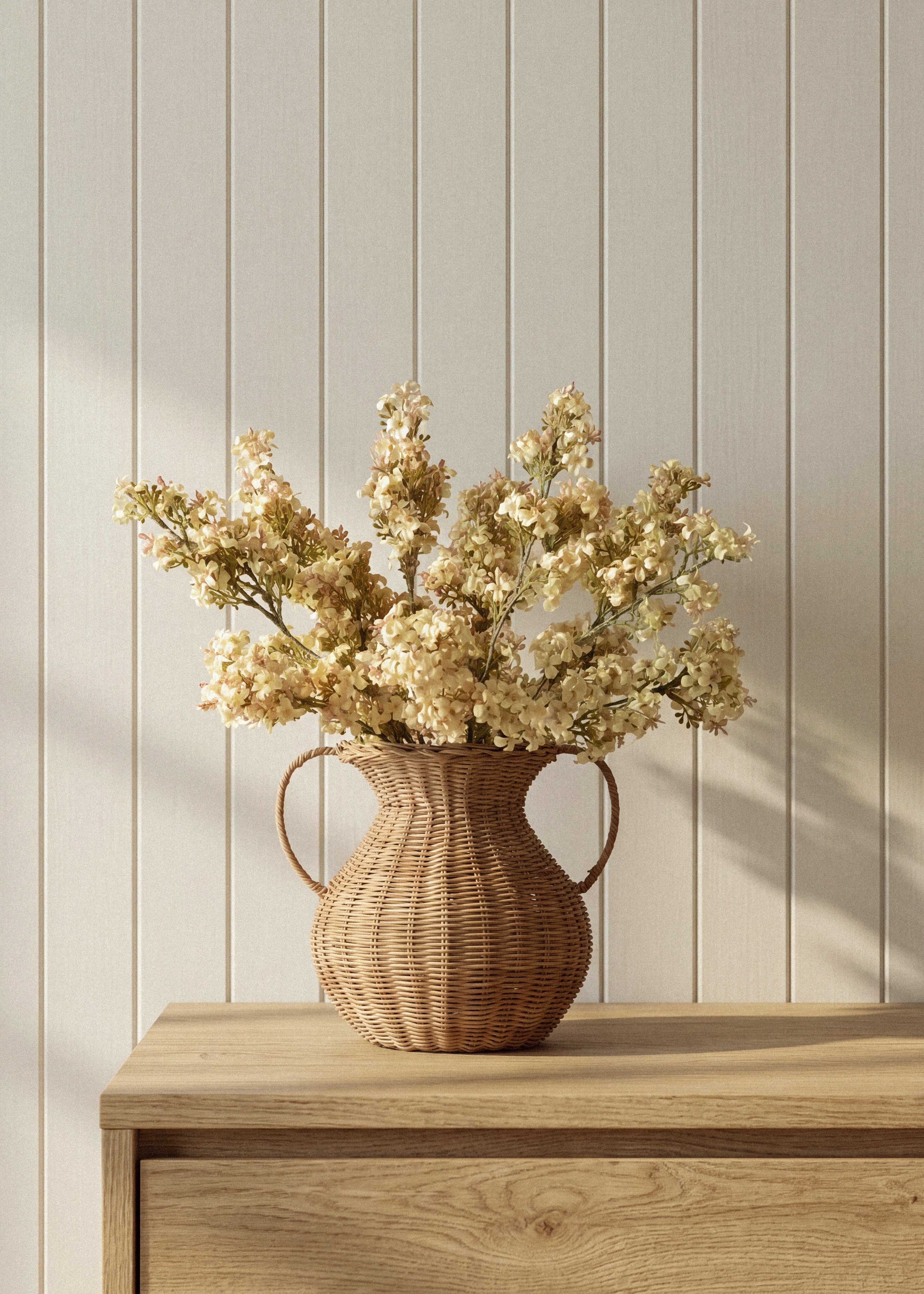 McGee & Co Rattan vase with dried flowers on a wooden surface against a light wooden panel wall
