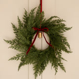 Green wreath with red ribbon and gold bulb on a beige wall
