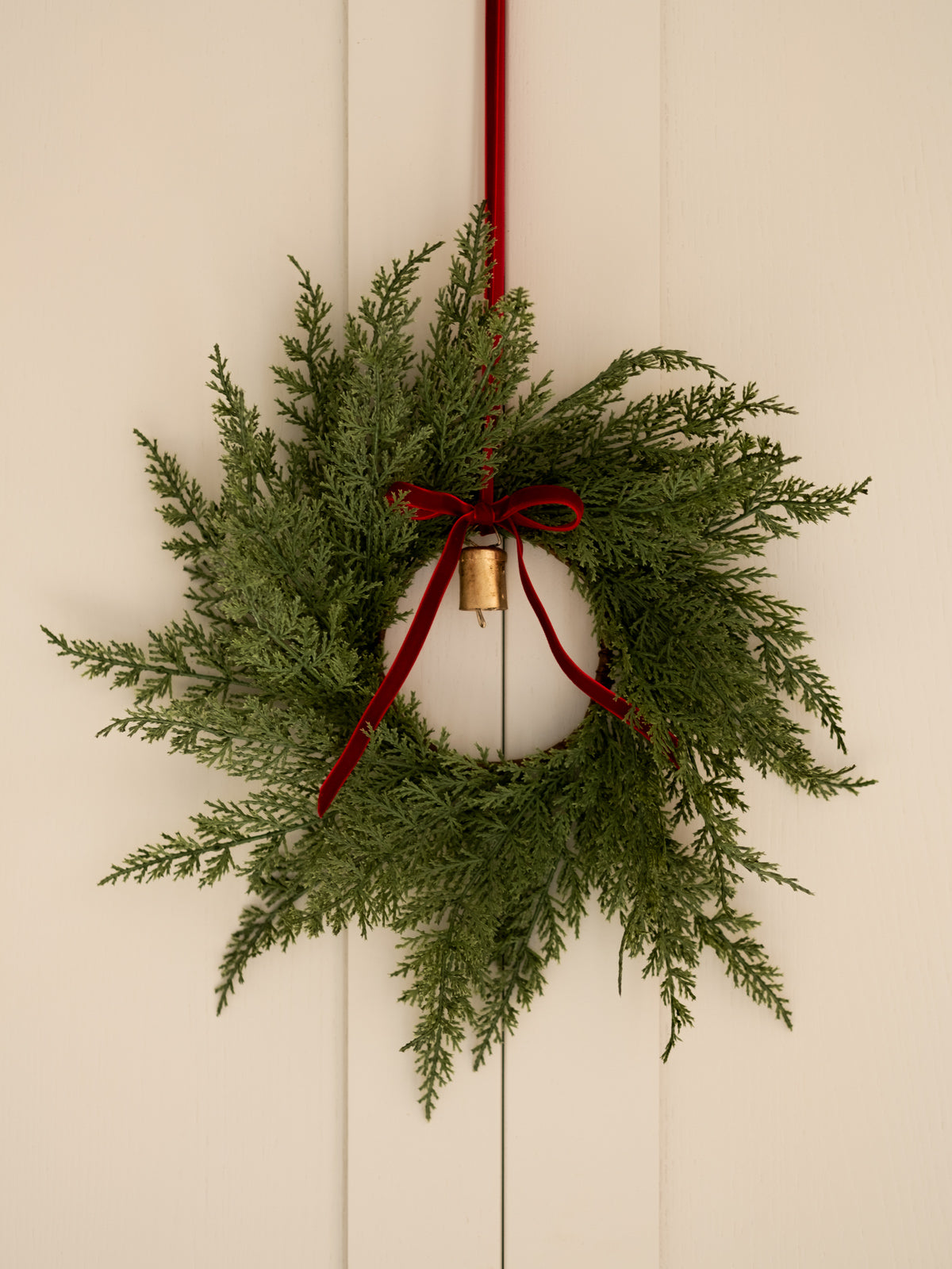 Green wreath with red ribbon and gold bulb on a beige wall