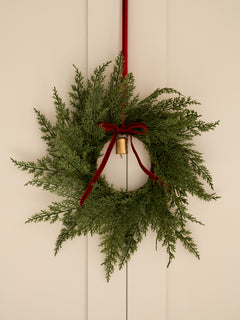 Green wreath with red ribbon and gold bulb on a beige wall