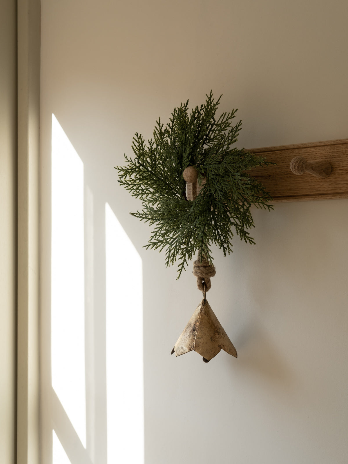 a green wreath being hung u on a wooden coat rack. a brass bell hanging from the hook