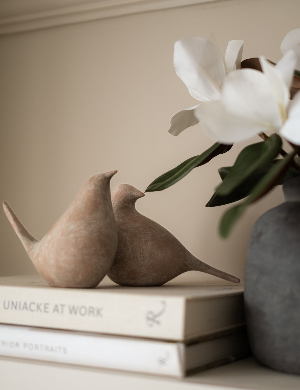 Two ceramic birds on books with a vase of white flowers in the background