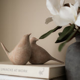 Two ceramic birds on books with a vase of white flowers in the background