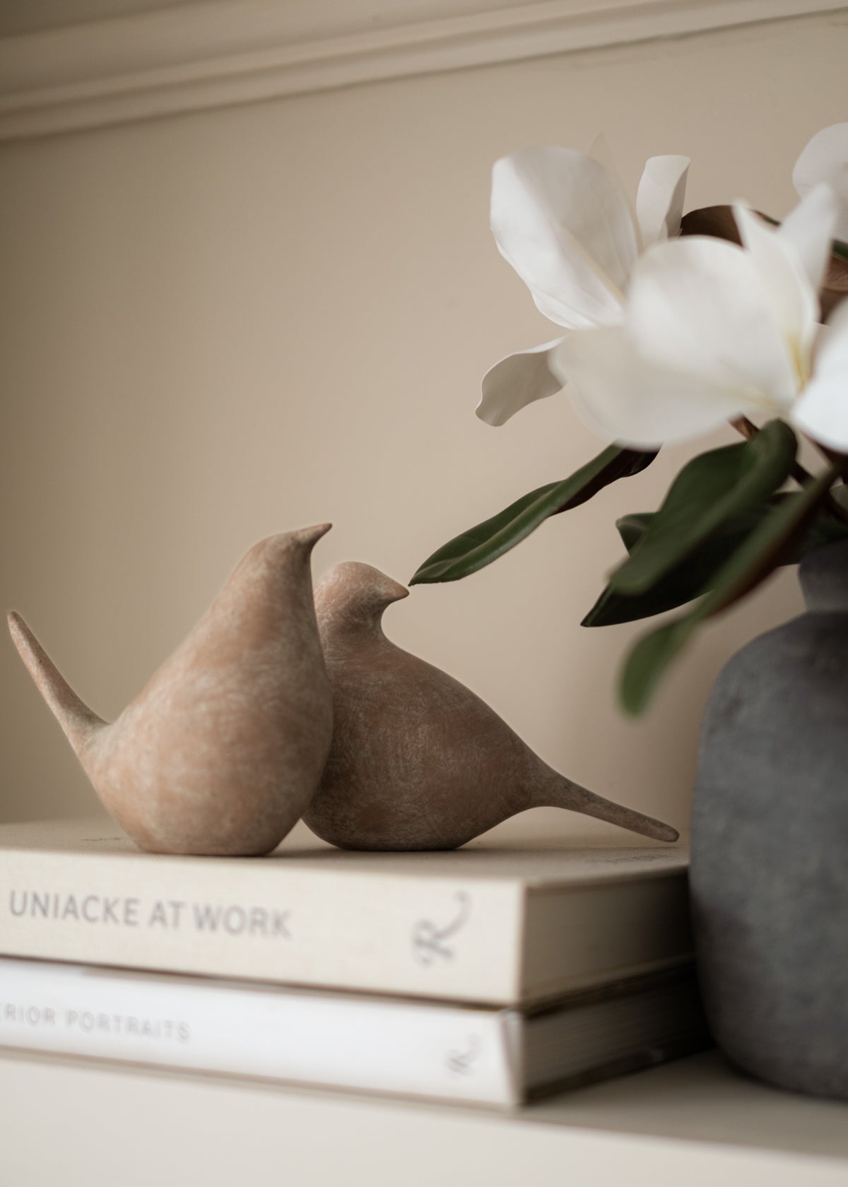 Two ceramic birds on books with a vase of white flowers in the background