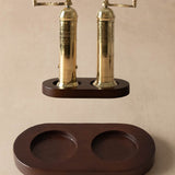 A pair of brass pepper mills with dark wood bases, shown with their matching dark wood storage tray on a neutral beige background.