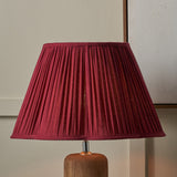 Lamp with a pleated red shade on a wooden base against a neutral wall.