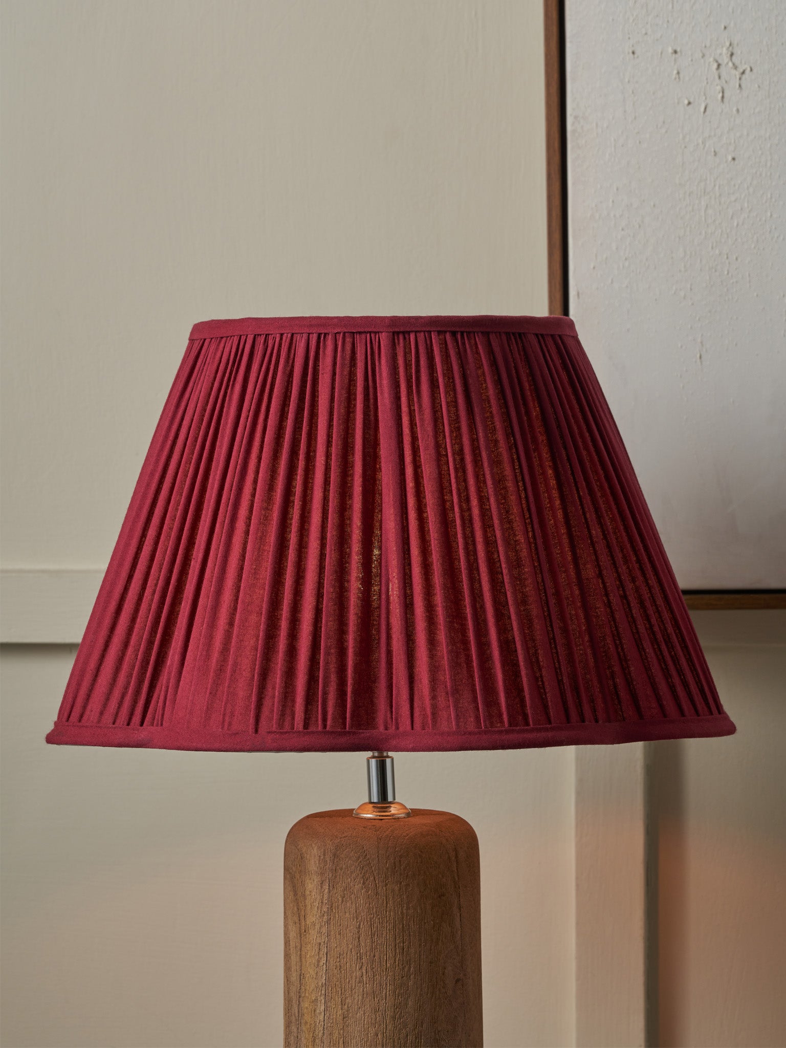 Lamp with a pleated red shade on a wooden base against a neutral wall.