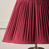 Red pleated lampshade on a wooden base against a beige background