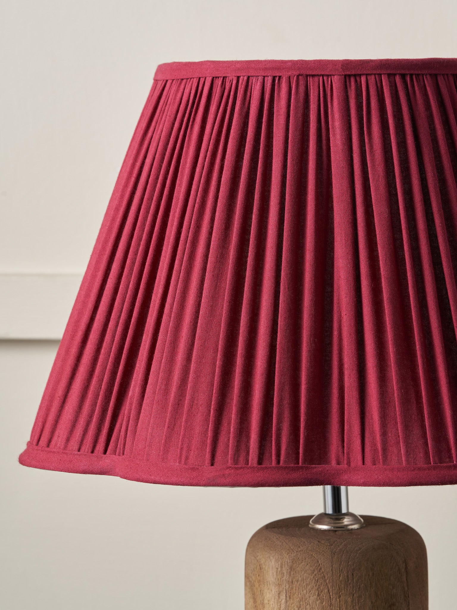 Red pleated lampshade on a wooden base against a beige background