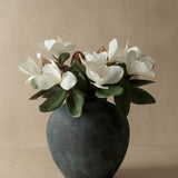 Faux white magnolia flowers in a dark gray vase on a beige background