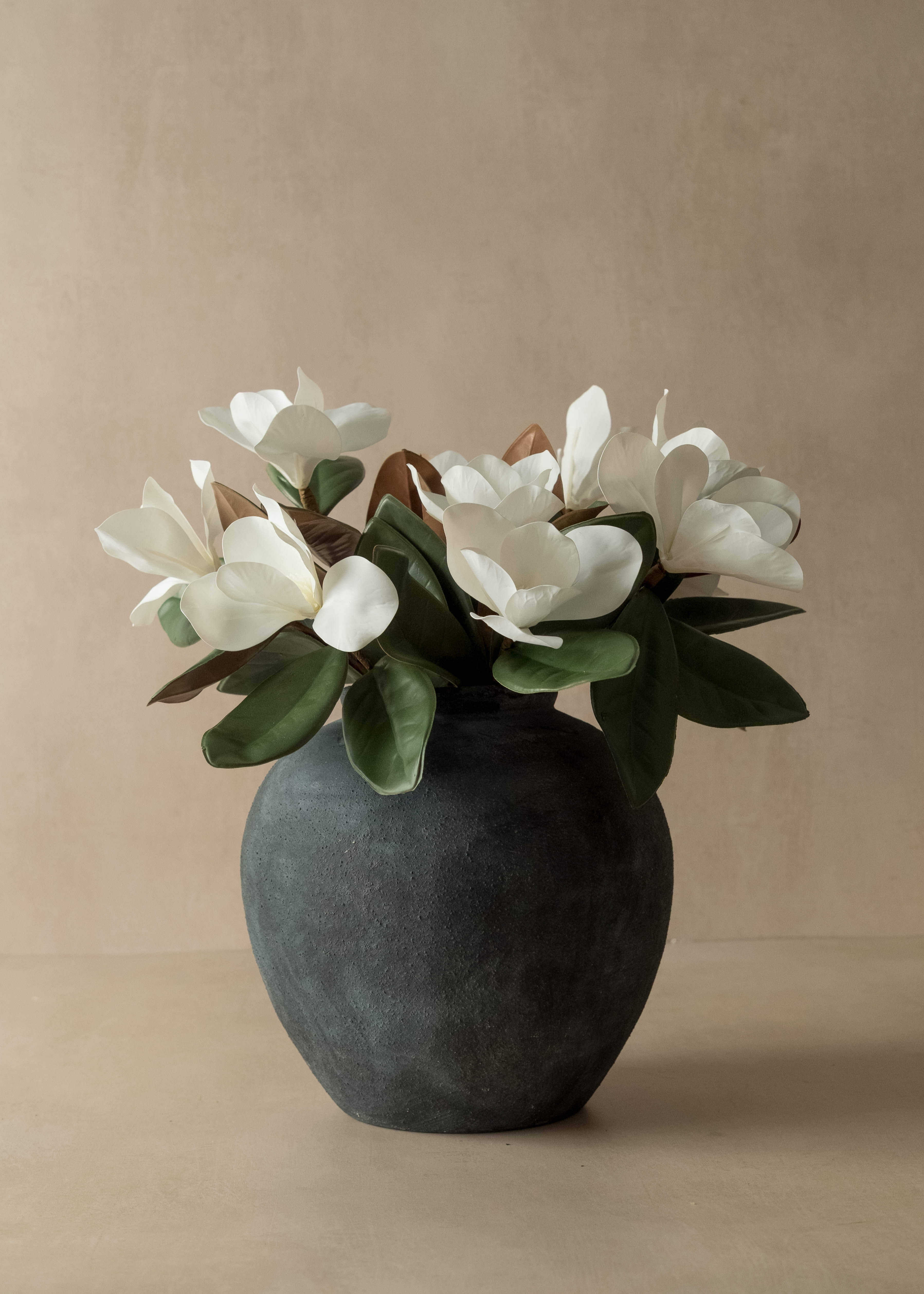 Faux white magnolia flowers in a dark gray vase on a beige background