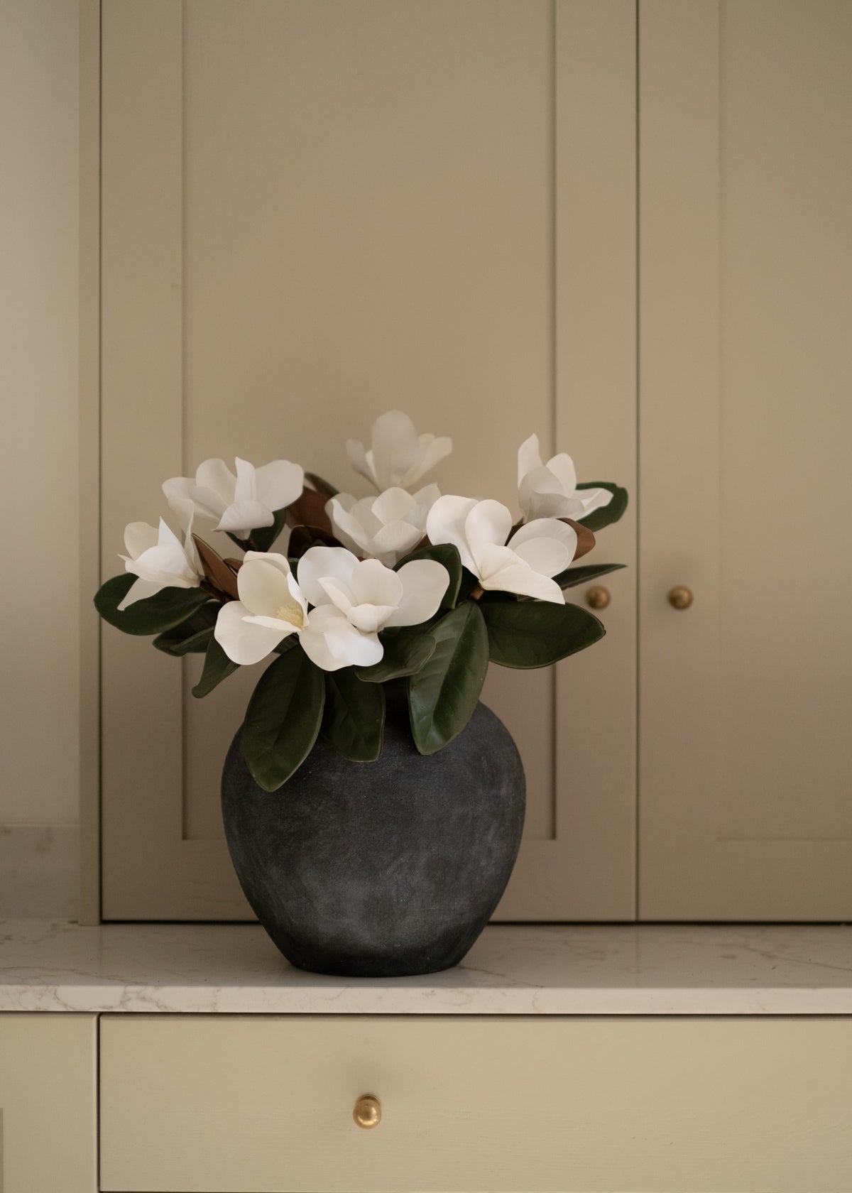 Faux flower arrangement in a dark vase on a neutral background